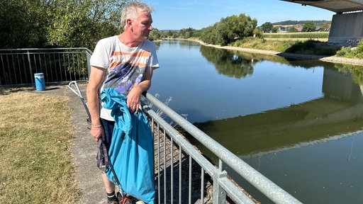 Ein Mann steht mit einem Müllsack am Ufer der Weser