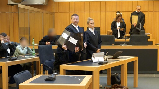 In einem Gerichtssaal sitzen mehrere Angeklagte und Juristen 
