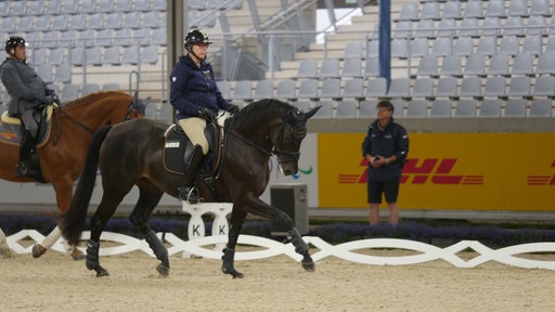 Zwei Personen reiten Pferde, während einer beobachtet