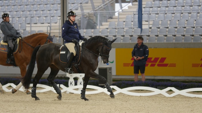 Zwei Personen reiten Pferde, während einer beobachtet