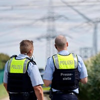 Zwei Polizisten stehen in einem Feld und blicken auf Strommasten im Hintergrund
