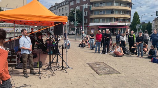 Zwei Personen reden vor einer Menschengruppe an einer Straße