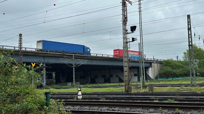 Seitenansicht auf die Brücke, auf der LKWs stehen und darunter Schienen verlaufen 