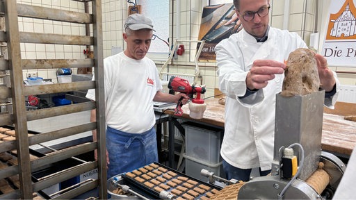 Ein mann gibt Teigmasse in eien Maschine. Unten kommen die fertigen Printen in einem Laufband heraus.