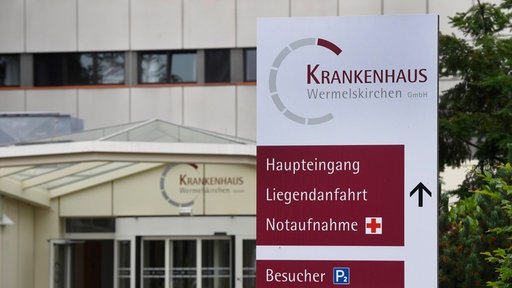 Ein Schild mit dem Logo der "Krankenhaus Wermelskirchen GmbH" steht vor dem Gebäude.