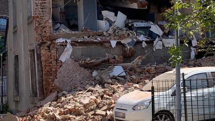Ein eingestürztes Haus, davor parkt ein Auto