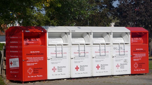 Rote und weiße Altkleidercontainer vor Bäumen