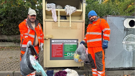 Zu sehen ist ein voller Altkleidercontainer und zwei Mitarbeiter der Stadt Düren in Arbeitskleidung.