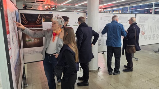 Mehrere Menschen stehen vor verschiedenen Stellwänden, einige zeigen auf Bilder