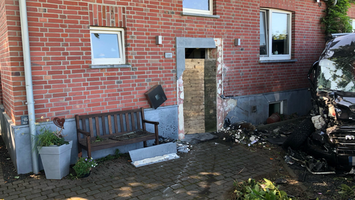 Eine beschädigtes Backsteinhaus. Daneben ein Auto mit kaputter Front.