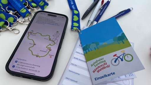 Auf einem Tisch liegt ein Handy mit dem Streckenverlauf und eine Stempelkarte