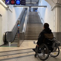 Wolfgang Thiems steht mit seinem Rollstohl vor den Treppen, die zum Bahngleis führen