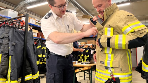 Zwei Männer in Uniform. Einer zieht gerade eine beige Uniform an