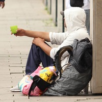 Ein obdachloser Mann sitzt mit einem Becher in der Hand in der Innenstadt