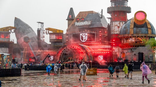 Die New Bill's Factory, eine Bühne beim Parookaville-Festival in Weeze, mit Menschen, die mit Ponchos durch den Regen laufen