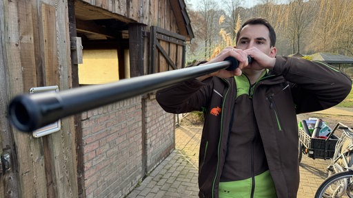 Ein Tierarzt im Tierpark hält ein Blasrohr an, um damit Impfungen zu verschießen.