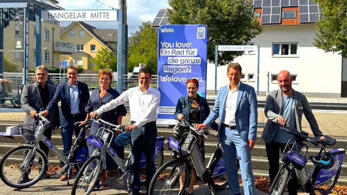 Eine Gruppe von sieben Personen steht mit Fahrrädern vor dem Bahnsteig der Station Hangelar Mitte.