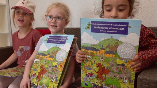 Drei Kinder schauen sich das Wimmelbuch an