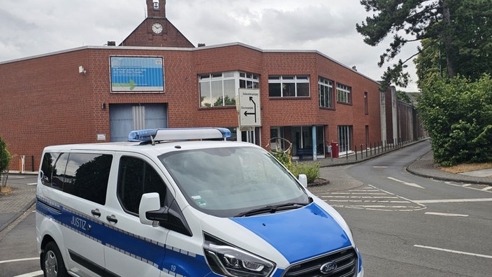 Ein Blau-weißes Spezialfahrzeug der Justizbehörde vor dem Gebäuder der JVA Siegburg.