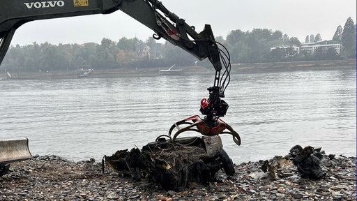 Ein Bagger bringt das Autowrack näher ans Ufer. Im Hintergrund fließt der Rhein.