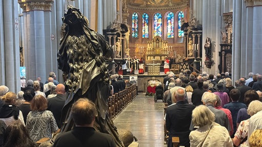 Zahlreiche Menschen sitzen und stehen in der Kirche Bonner Münster während einer Gedenkfeier. Vor dem Altar sind ein Kranz und ein gerahmtes Porträt von Kondrad Beikircher aufgestellt.