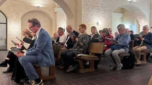 Eine Gruppe von Menschen sitzen im Gottesdienst und halten ihre Gesangsbücher in der Hand
