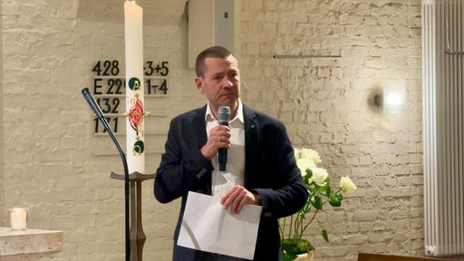Mann steht in der Kirche und hält ein Mikrofon in der Hand