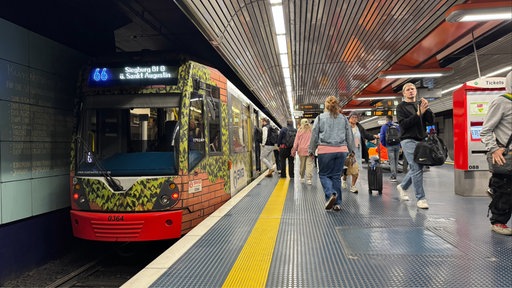 Bahn fährt in Station ein und Leute steigen ein