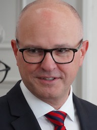 Torsten Janßen, der neue Prinz von Bonn, ist im Gespräch mit einem anderen Mann. Thorsten I. trägt eine schwarze Brille, einen Anzug und hat eine Glatze.