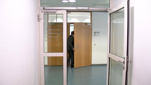 Mann geht durch eine Tür. Vor der Tür ist noch eine Glastür.