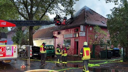 Feuerwehr-Leute stehen vor Haus von dem Qualm aufsteigt