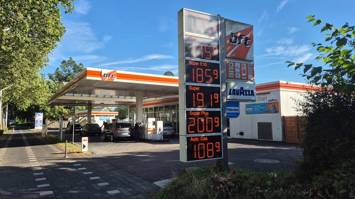 Eine orangene Tankstelle mit Anzeigetafel und Bäumen links und rechts im Hintergrund. 