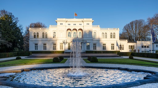Springbrunnen im Vordergrund, weiße Villa im Hintergrund