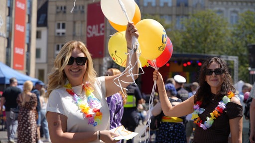 Zwei Frauen mit Sonnenbrillen halten bunte Luftballons in ihren Händen.