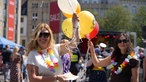Zwei Frauen mit Sonnenbrillen halten bunte Luftballons in ihren Händen.