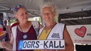 Zwei Frauen von den Omas gegen Rechts tragen weiße Westen und halten ein Nummernschild ain den Händen.