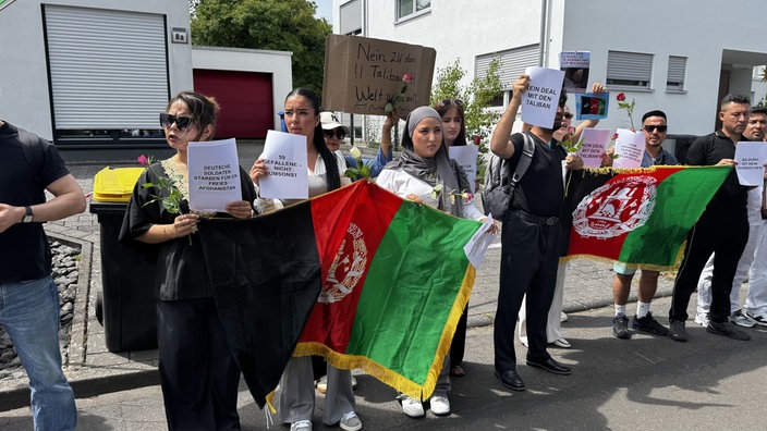 eine Gruppe Demonstrierende mit Schildern und Afghanistan-Flagge stehenh nebeneinander