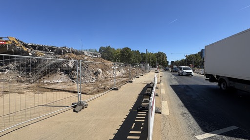 Zu sehen ist ein Teil der Nordbrücke Bonn. Rechts fahren Autos über die Brücke, in der Mitte steht ein Baustellenzaun und links im Bild die Baustelle.