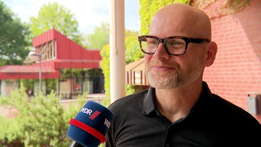 Ein Mann mit Brille spricht in ein blaues WDR-Mikrofon.