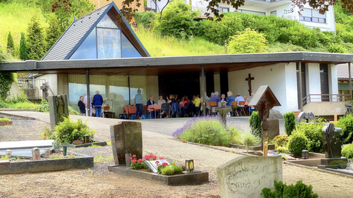 Unter dem Vordach der Trauerhalle auf dem Friedhof sind die Besucherinnen und Besucher des Kaffeeklatsches zusammen gekommen
