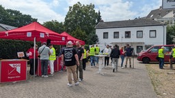 Haribo-Mitarbeiter stehen in einer Hofeinfahrt. Links sind Infostände der Gewerkschaft NGG aufgebaut. Einige Anwesende tragen Warnwesten.