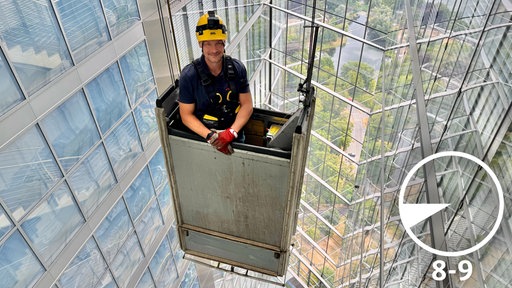 Techniker Thorsten Klanke steht in einer Gondel, die im Post Tower zwischen Glasfassaden schwebt. 