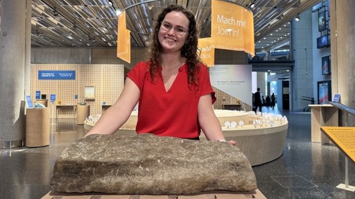 Lotta Westdorf schaut in die Kamera. Vor ihr ein Stein
