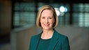 Eine Frau mit kurzen blonden Haaren und dunklem Blazer lächelt in die Kamera.