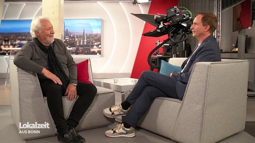 Konrad Beikircher und Moderator Ralf Henscheidt sitzen im Fernsehstudio der Lokalzeit aus Bonn und unterhalten sich.