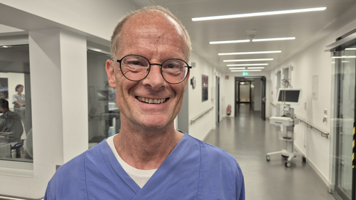 Krankenpfleger Tom Rey im St. Josef Hospital als Portrait mit einem Gang des Krankenhauses im Hintergund 
