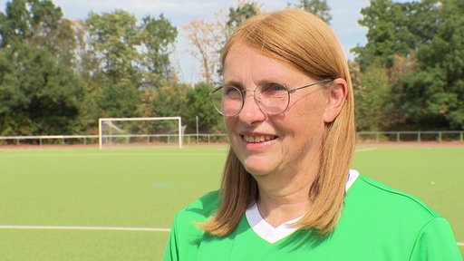 Eine Frau ine einem grünen T-Shirt und Brille spricht in die Kamera.