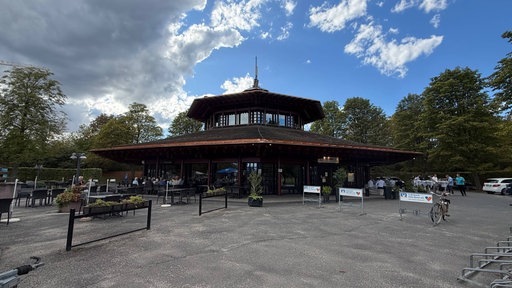 Ein Gebäude mit spitzem Dach. Davor Asphalt. Im Hintergrund ist blauer Himmel. 