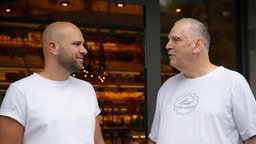 Michael Markmann und Uli Linnemann stehen vor der Bäckerfiliale in Bonn-Rüngsdorf