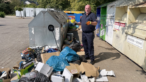 Ein Mann steht neben mehreren Müllcontainern, im Vordergrund befindet sich ein Müllberg.